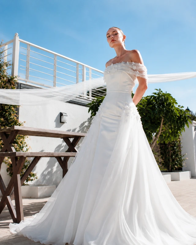 White off-the-shoulder bridal gown with a fitted silhouette and a flared skirt and train., photo 1